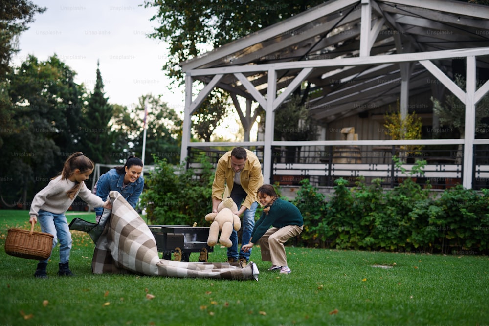 バスケットと毛布を持った幸せな若い家族が、レストランエリアで屋外でピクニックをする。