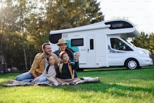 A happy young family with two children ltaking selfie with caravan at background outdoors.