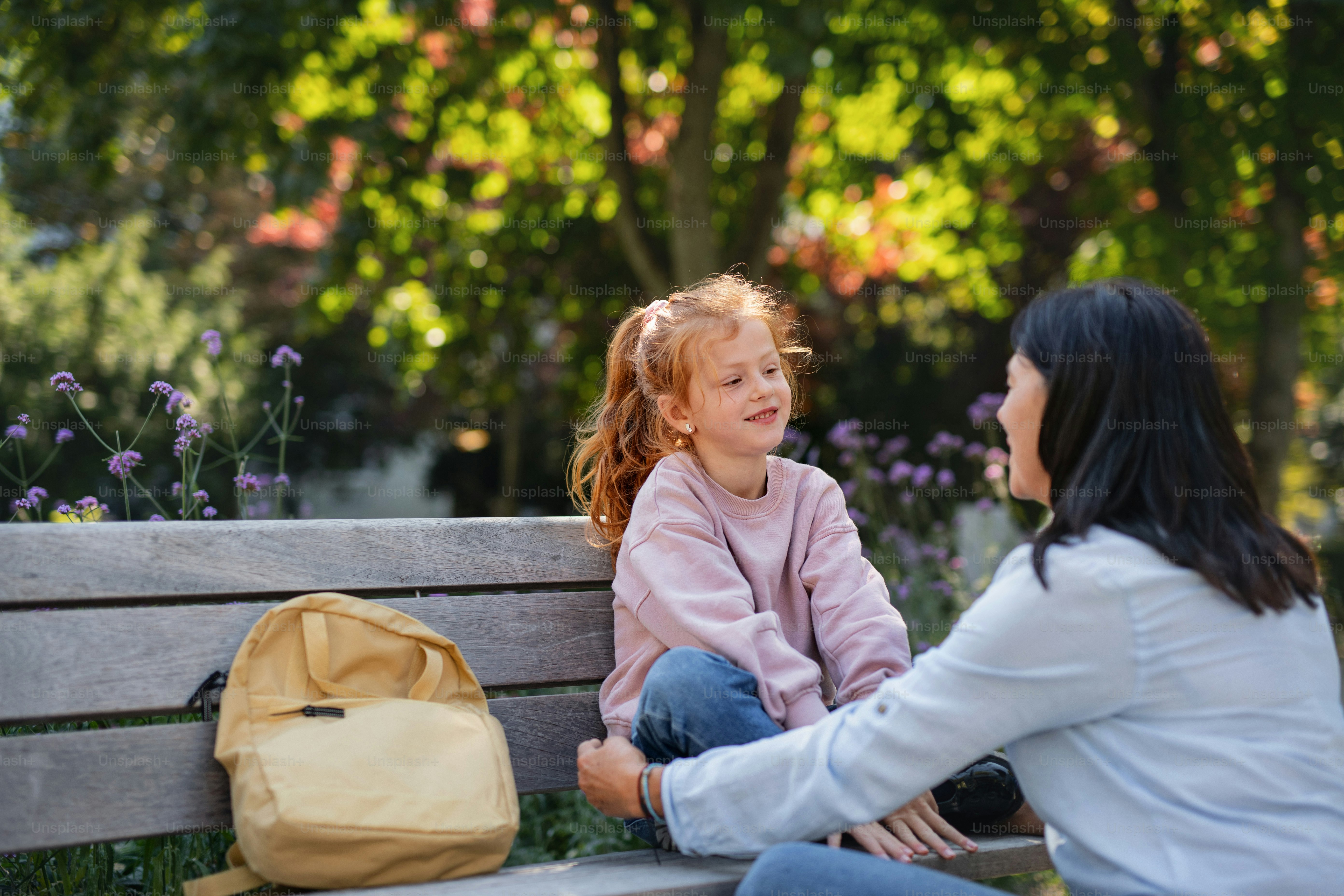 A senior woman squatting and talking to granddaughter outdoors on bench in park