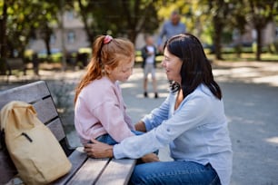 Una donna anziana accovacciata e parla con la nipote all'aperto sulla panchina del parco.