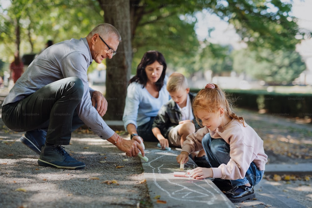 Una pareja mayor con nietos dibujando con tizas en el pavimento al aire libre en el parque.
