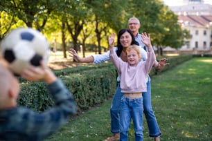 Happy little children with grandparents playing with a football outdoors in park