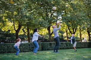 Happy little children with grandparents playing with a football outdoors in park