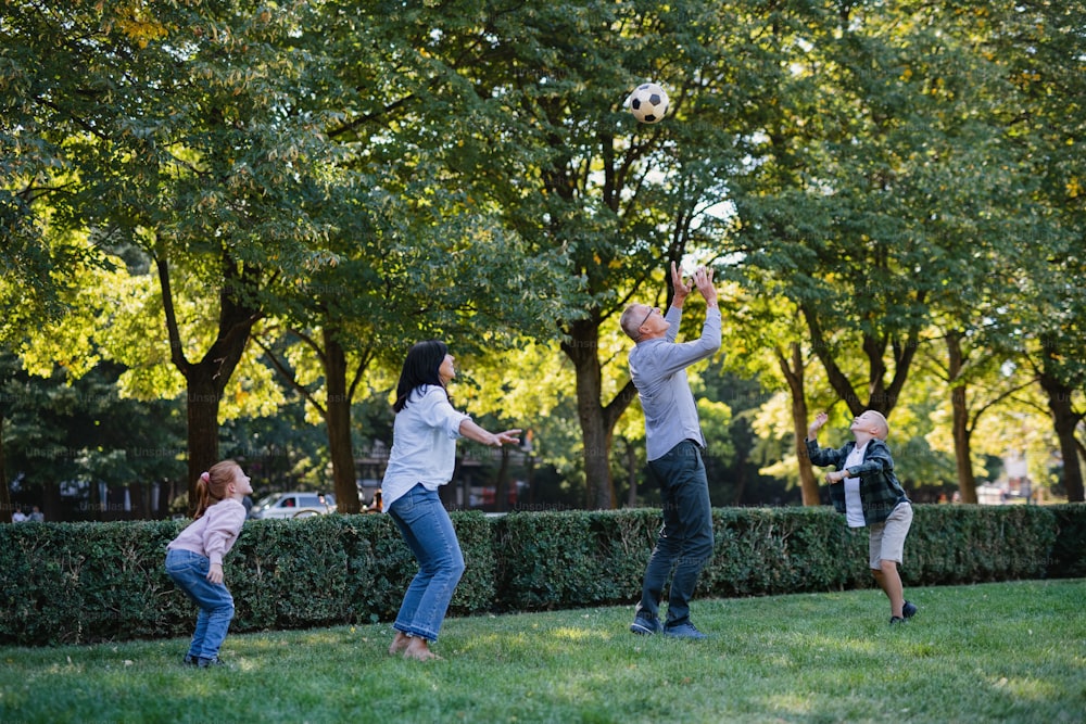 Niños pequeños felices con abuelos jugando con una pelota de fútbol al aire libre en el parque