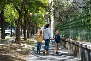 A rear view of grandmother taking grandchildren home from school, walking outdoors in street.