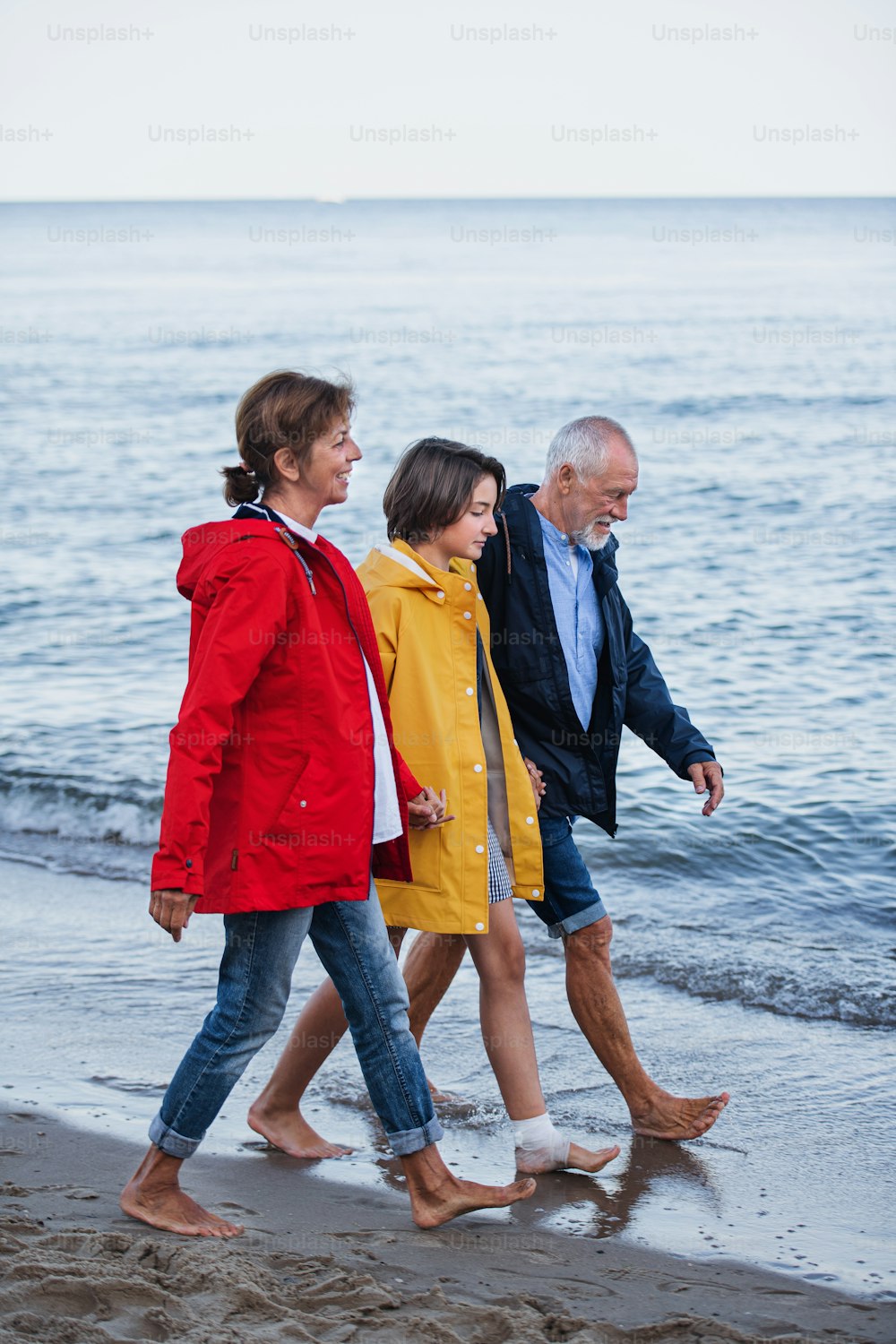 Una pareja mayor tomada de la mano con su nieta preadolescente y caminando por la playa de arena.