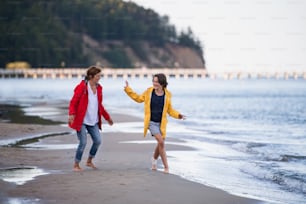 Uma mulher idosa e sua neta pré-adolescente correndo e se divertindo na praia.