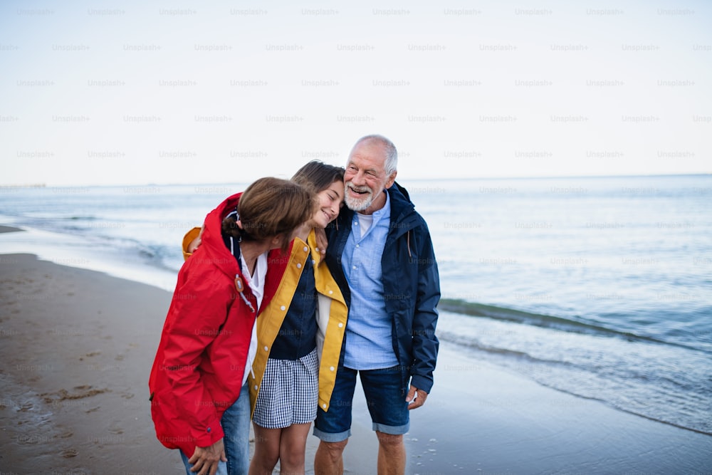 A senior couple and their preteen granddaughter hugging when walking on sandy beach.