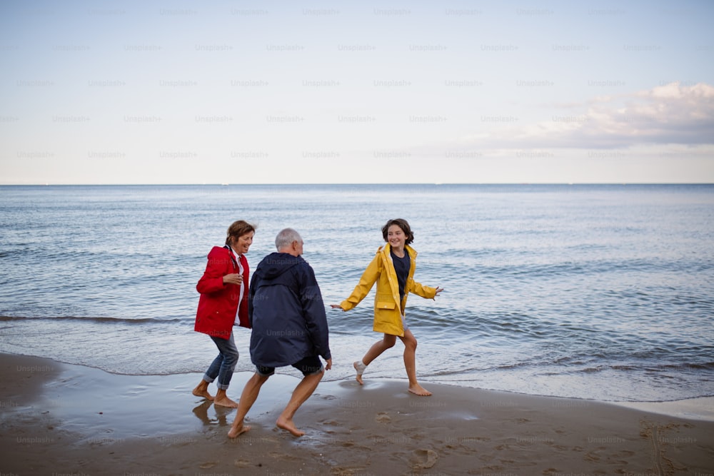 A senior couple and their preteen granddaughter running and having fun on sandy beach.