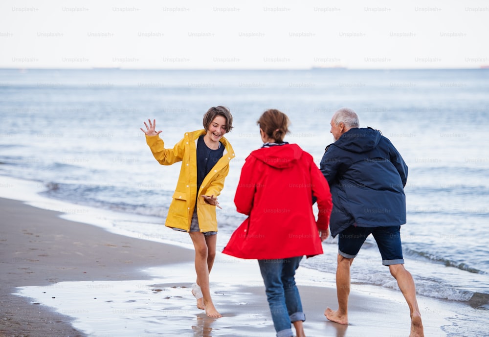 A senior couple and their preteen granddaughter running and having fun on sandy beach.