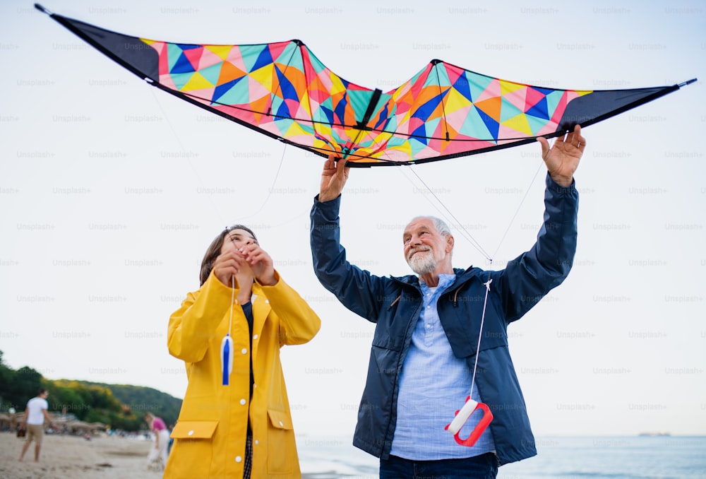 A low angle view of preteen girl and her grandfather playing with kite on sandy beach.