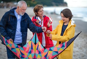 Grandparents with a preteen girl preparing kite for flying on sandy beach.