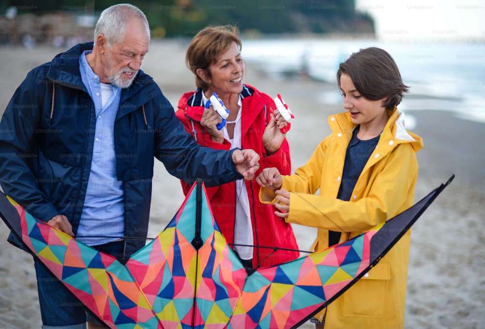 Grandparents with a preteen girl preparing kite for flying on sandy beach.