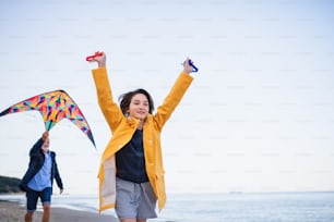 A low angle view of preteen girl and her grandfather playing with kite on sandy beach.