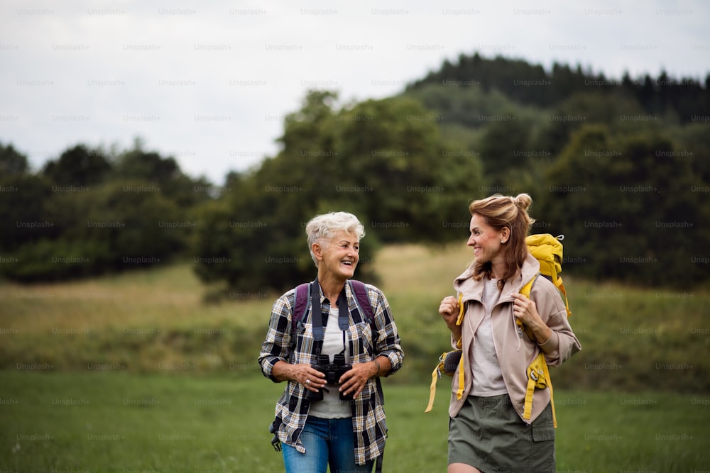 An active senior woman with binoculars hiking with her adult daughter outdoors in nature.