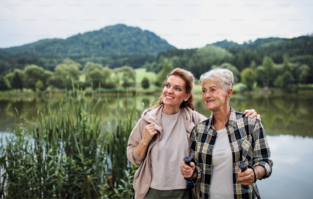 A happy senior mother embracing with adult daughter when standing by lake outdoors in nature