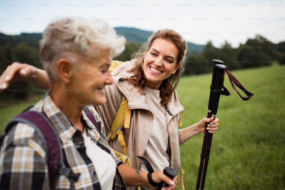Una donna adulta media felice con bastoncini da trekking che fanno escursioni con madre anziana attiva all'aperto nella natura.