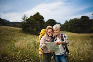 A happy mid adult woman with active senior mother hiking and looking at map outdoors in nature.