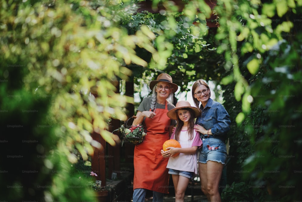 A happy little farmer girl with mother and grandmother looking at camera outdoors at garden