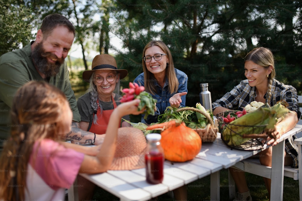 A happy family of farmers sitting by the table and looking at their harvest outdoors at community farm.
