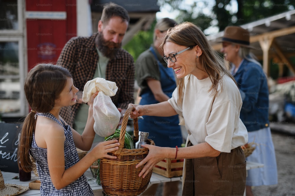 A little girl buying organic vegetables outdoors at community farmers market.