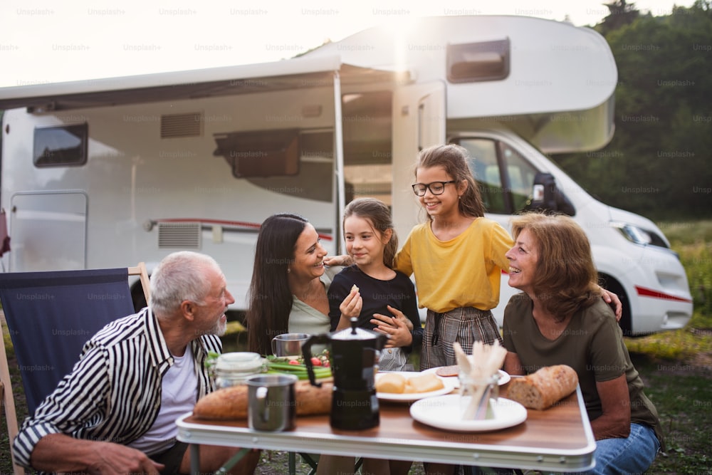 Eine Mehrgenerationenfamilie, die mit dem Auto im Freien sitzt und isst, Wohnwagenurlaub.