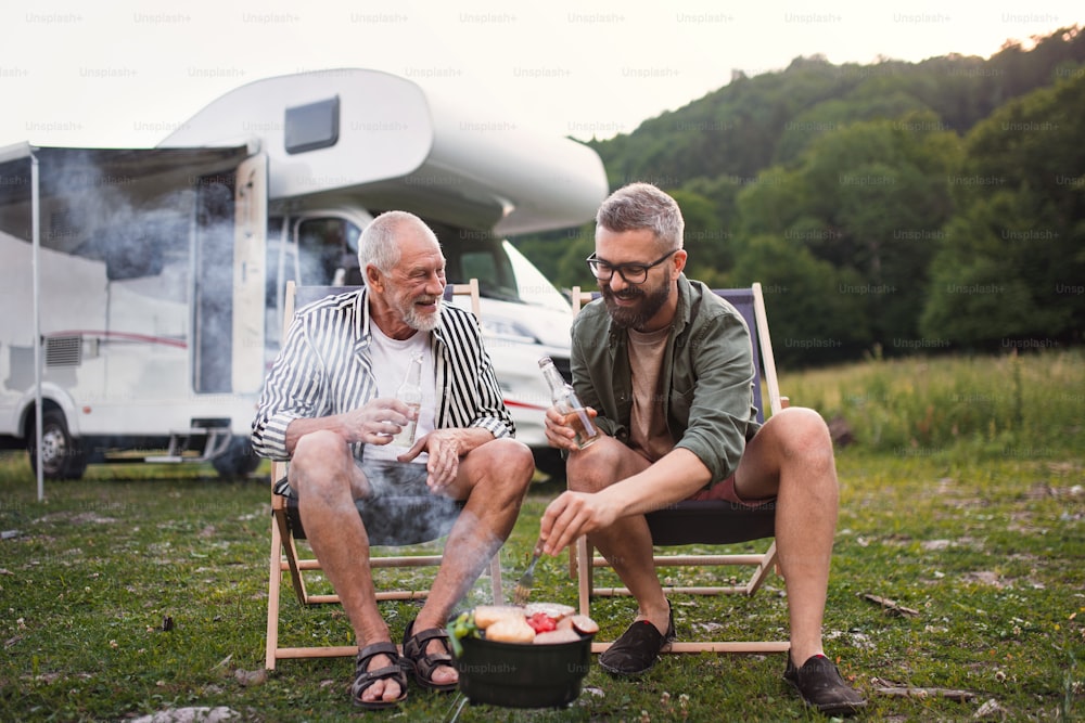 Un homme mûr avec un père âgé parlant au camping en plein air, barbecue en caravane voyage de vacances.