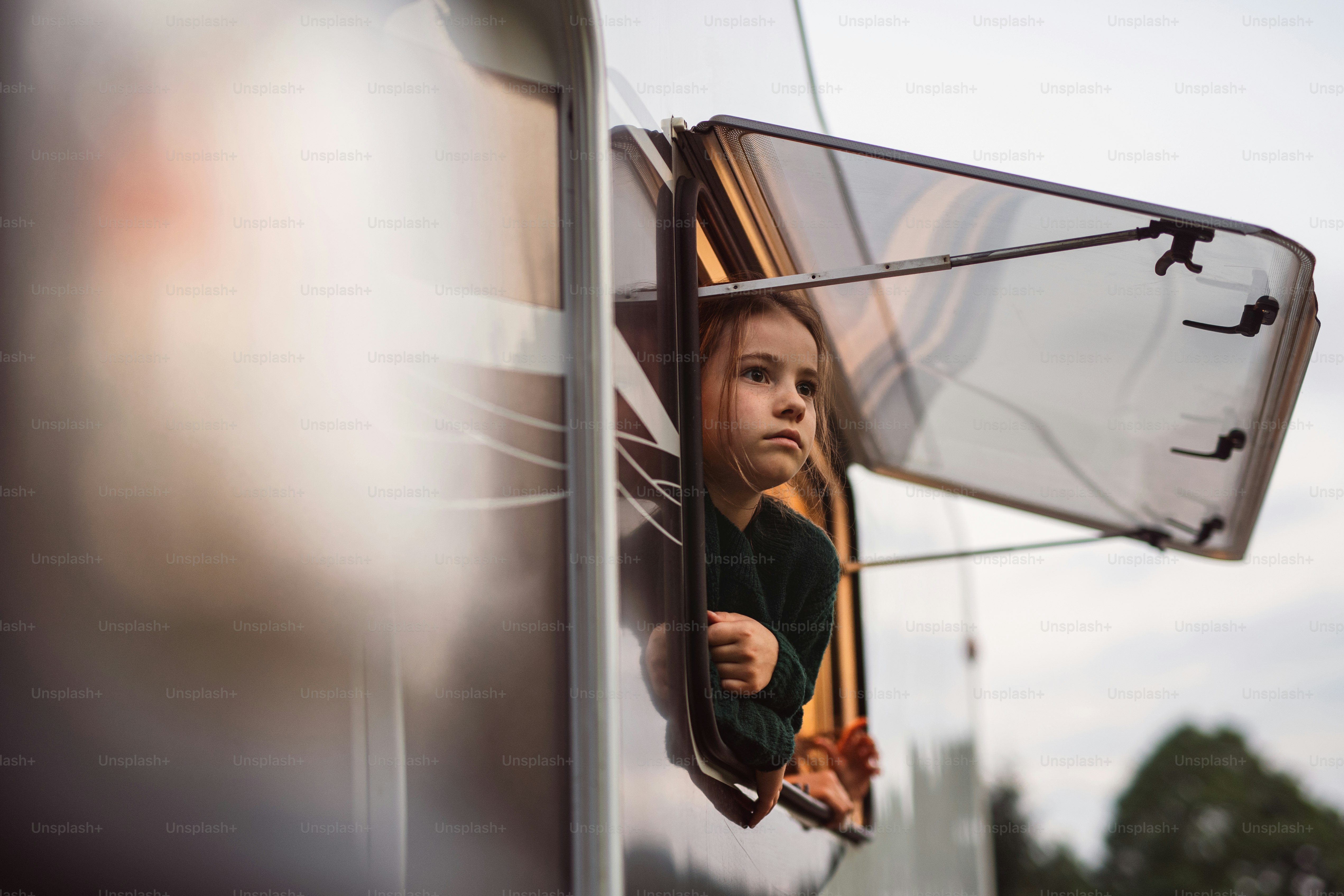 Una niña pequeña mirando a través de la ventana de la caravana, viaje de vacaciones en familia.