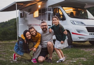 Front view of happy family looking at camera outdoors at dusk, caravan holiday trip.