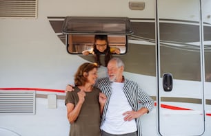 A senior couple with granddaughter standing by car, caravan family holiday trip.