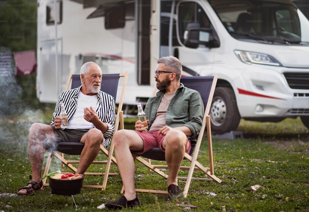 노부인 아버지와 함께 야외 캠핑장에서 이야기를 나누는 성숙한 남자, 캐러밴 휴가 여행에서 바비큐를 하고 있다.