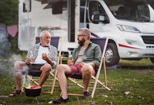Ein reifer Mann mit älterem Vater, der sich auf dem Campingplatz im Freien unterhält, grillt auf einer Wohnwagenurlaubsreise.