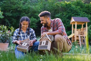 Un joven feliz con una hermana pequeña sosteniendo hoteles de insectos al aire libre en el patio trasero, riendo.