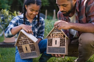A happy young man with small sister holding bug hotels outdoors in backyard.