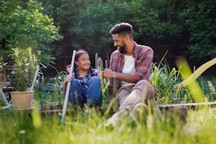 Happy young father with small daughter working outdoors in backyard, a gardening concept.