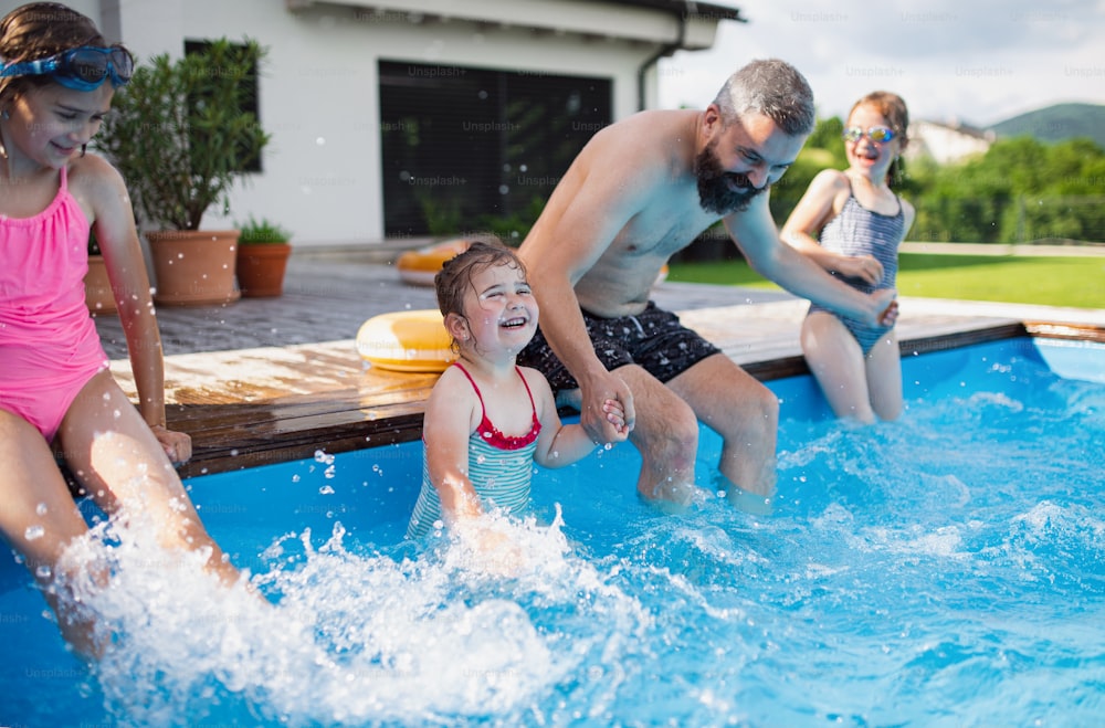 A father with three daughters outdoors in the backyard, playing in swimming pool.
