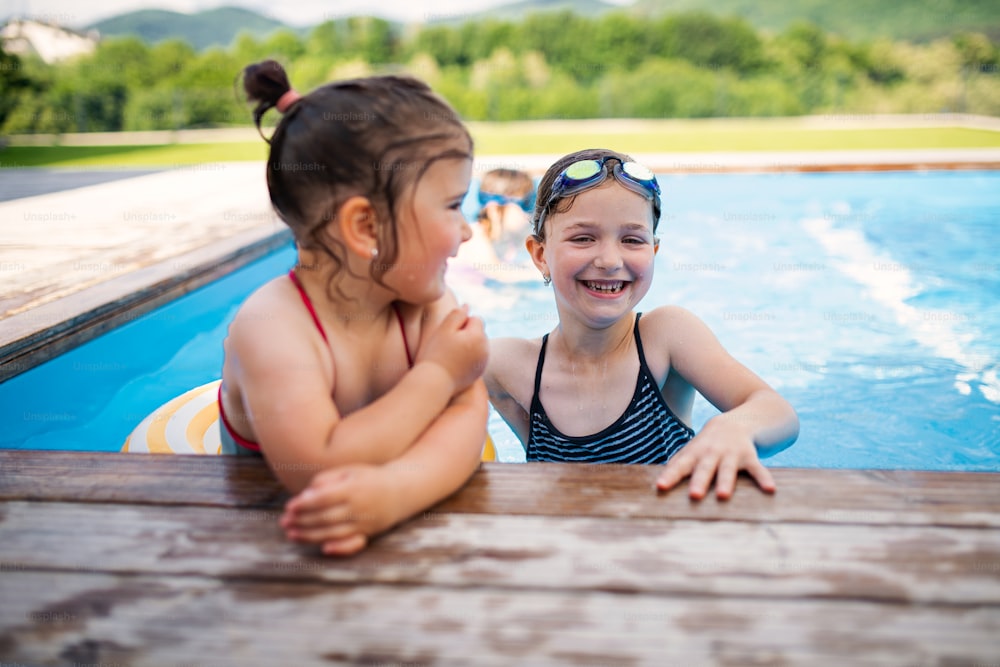Retrato de dos hermanas niñas al aire libre en el patio trasero, hablando en la piscina.