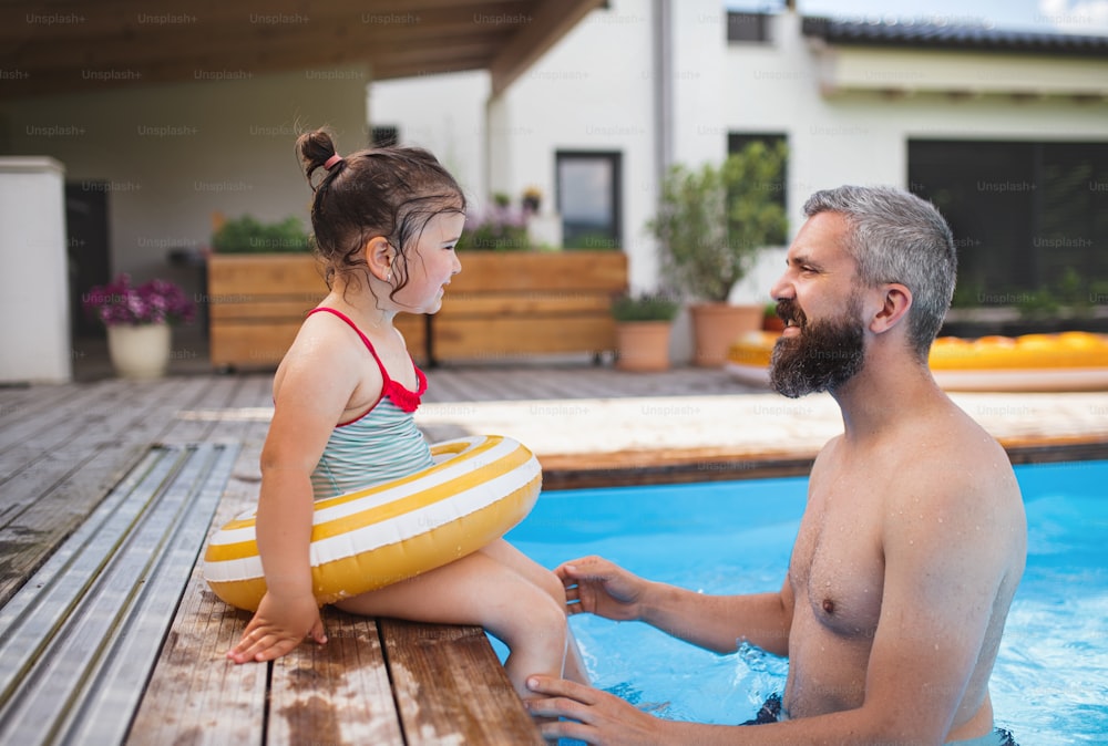 Father with happy daughter outdoors in the backyard, playing in swimming pool.