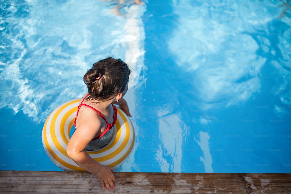 Une vue de dessus de petite fille à l’extérieur dans la cour, avec anneau en caoutchouc dans la piscine.