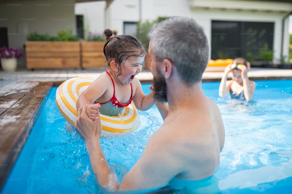 Father with happy daughters outdoors in the backyard, playing in swimming pool.