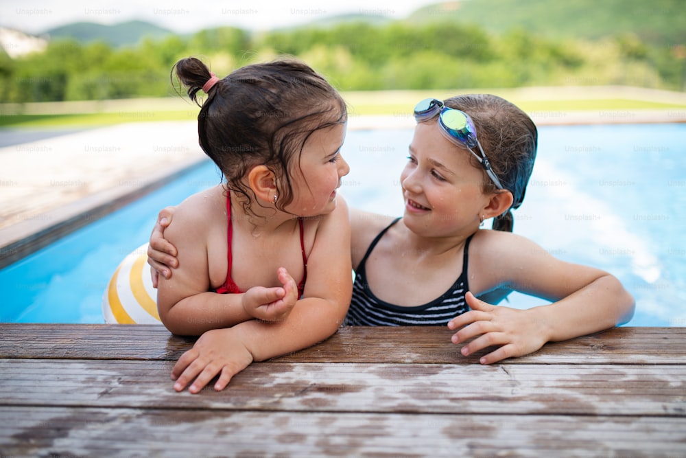 Portrait de deux petites filles sœurs dehors dans la cour, discutant dans la piscine.