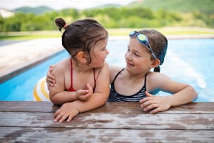 Portrait of two small girls sisters outdoors in the backyard, talking in swimming pool.
