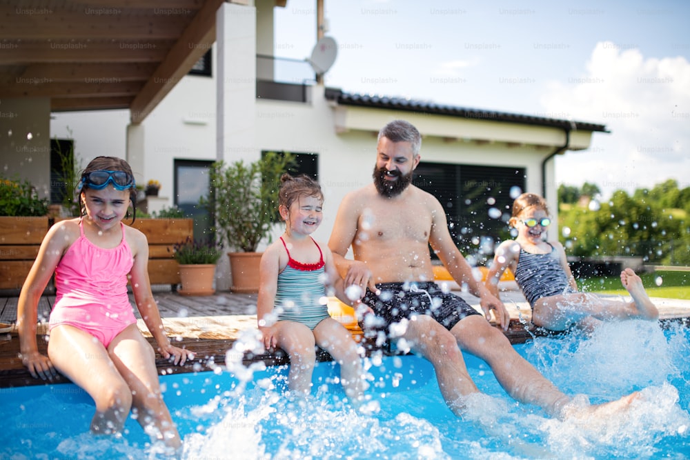 A father with three daughters outdoors in the backyard, sitting by swimming pool.