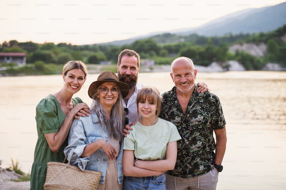 Une famille multigénérationnelle heureuse en promenade au bord du lac pendant les vacances d’été, regardant la caméra.