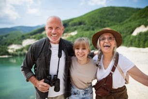 Una niña preadolescente feliz con sus abuelos en un viaje de senderismo en vacaciones de verano, mirando a la cámara.