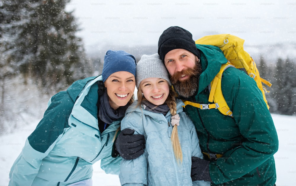 A portrait of happy family with small daughter looking at camera outdoors in winter nature, Tatra mountains Slovakia.