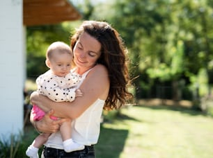 Happy woman holding baby daughter outdoors in backyard. Copy space.
