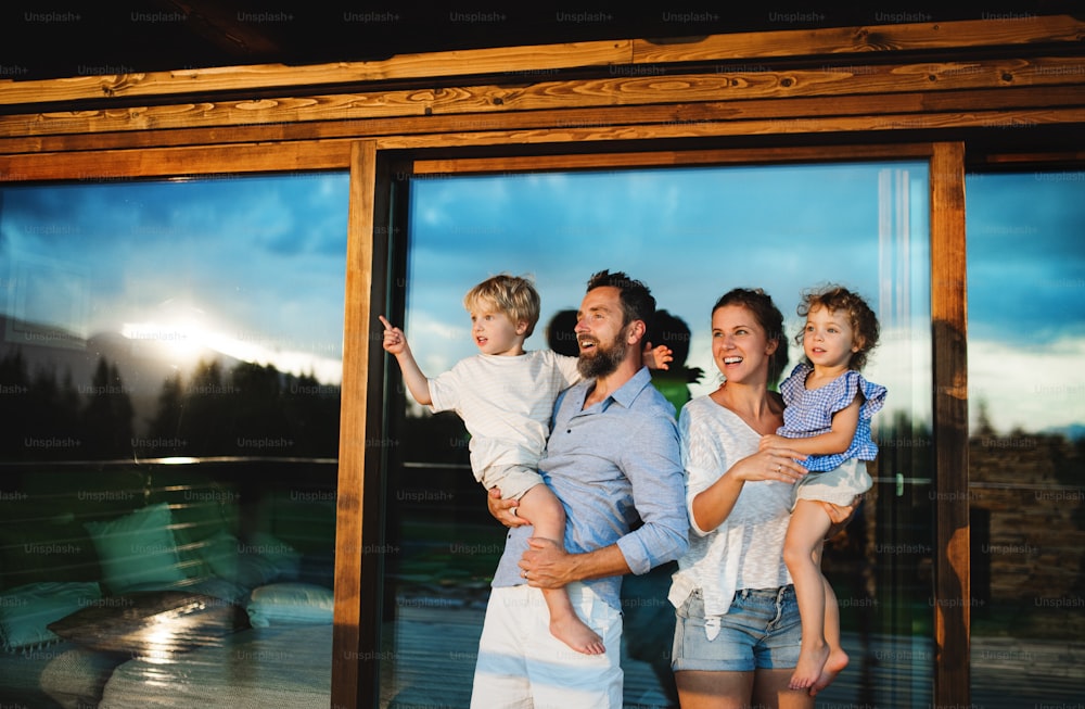 Famiglia felice con bambini piccoli in piedi sul patio da cabina di legno, concetto di vacanza nella natura.
