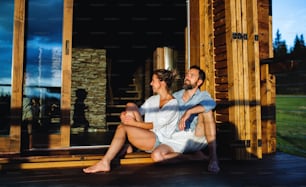 Portrait of happy couple sitting on patio of wooden cabin, holiday in nature concept.