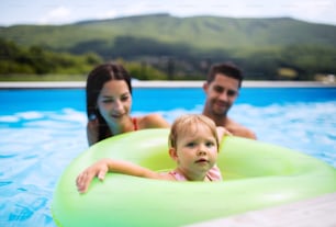 뒤뜰 정원에 있는 야외 수영장에서 작은 딸과 함께 행복한 젊은 ��가족.